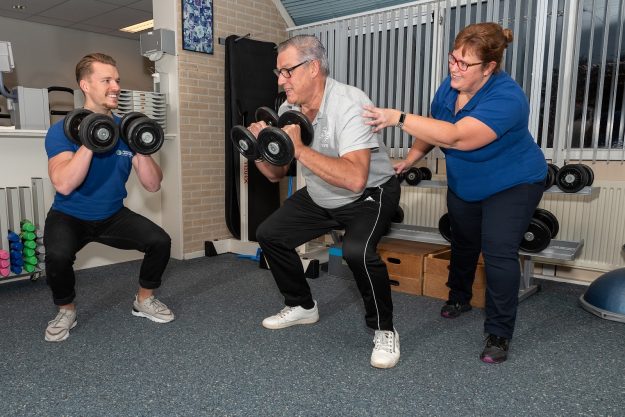 Fysiotherapie Lansingerland Berkel en Rodenrijs – hoge bloeddruk Peter in zijn witte shirt oefent samen met fysiotherapeuten Sven en Suzanne aan zijn hoge bloeddruk in de oefenzaal
