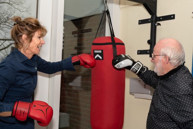 Fysiotherapie Lansingerland Berkel en Rodenrijs – sporten en bewegen met parkinson Willem met zwarte bokshandschoenen wordt geholpen door een fysiotherapeut van Fysiotherapie Lansingerland met rode bokshandschoenen voor sporten en bewegen met parkinson