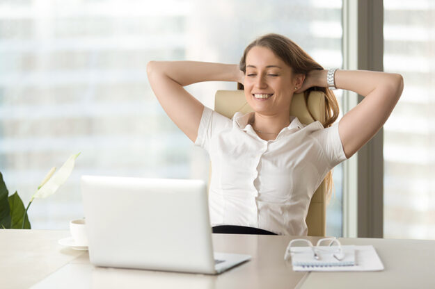 Hoge rugpijn Vrouw voorkomt hoge rugpijn en zit op een stoel aan haar bureau terwijl ze glimlacht en tevreden is met haar werk.