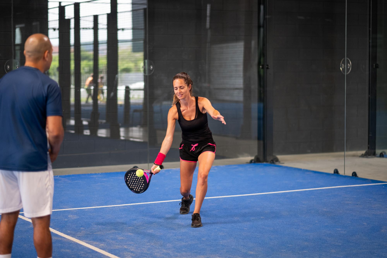 Sport Een vrouw staat op een sportveld en speelt de sport padel. Een man staat aan de zijlijn en kijkt naar haar.