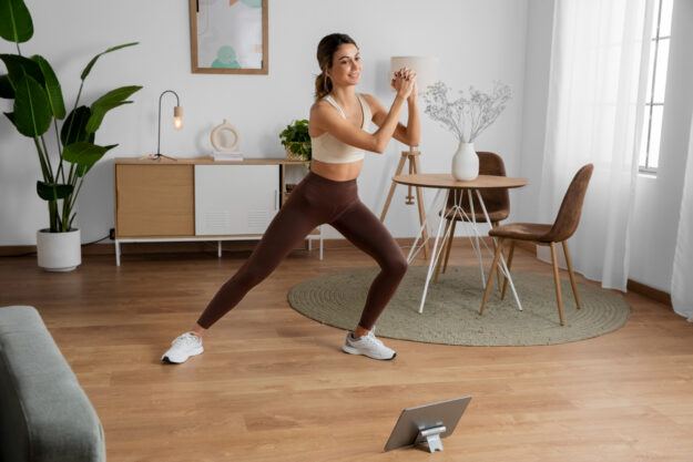 lichaamsgewicht Een vrouw staat in een woonkamer. Ze traint met haar lichaamsgewicht. Ze heeft sportkleding aan.